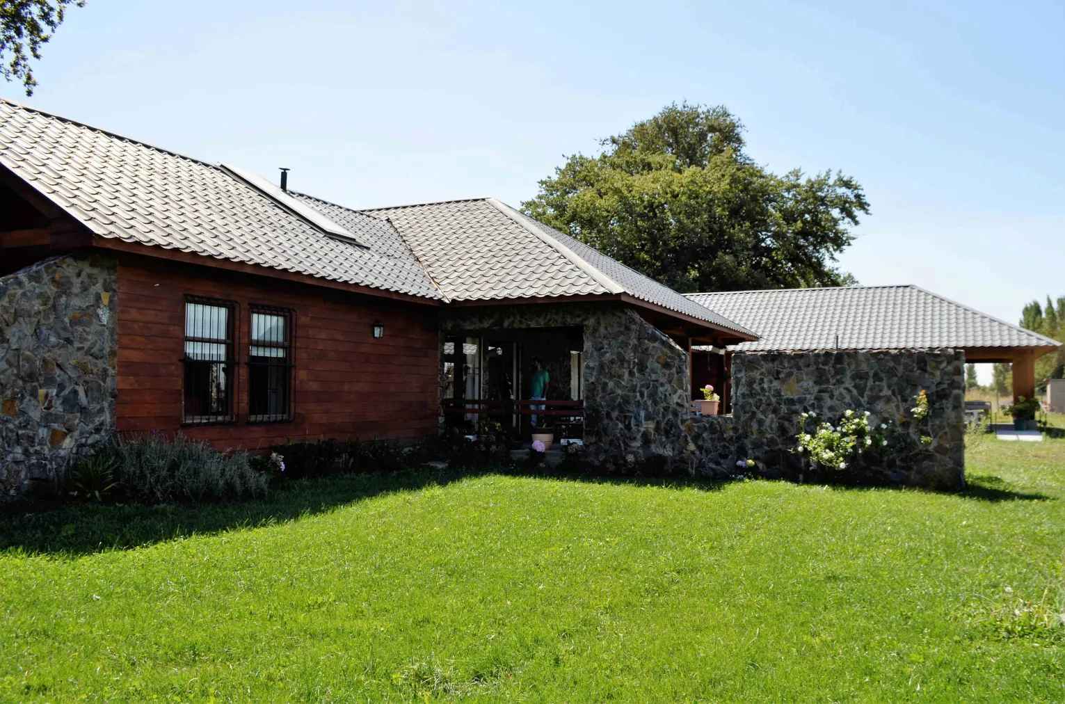Exterior de la casa de madera y piedra, con pasto y árboles alrededor