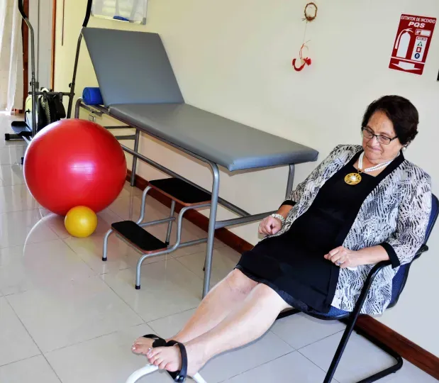 Sala de kinesiología con camilla y balón terapéutico, y una residente sentada