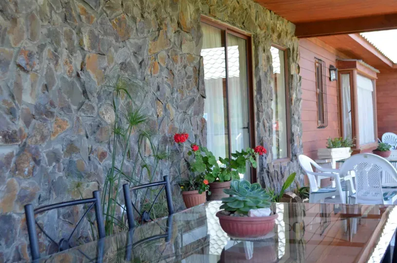 Terraza junto a un muro de piedra, con mesas y maceteros con flores rojas